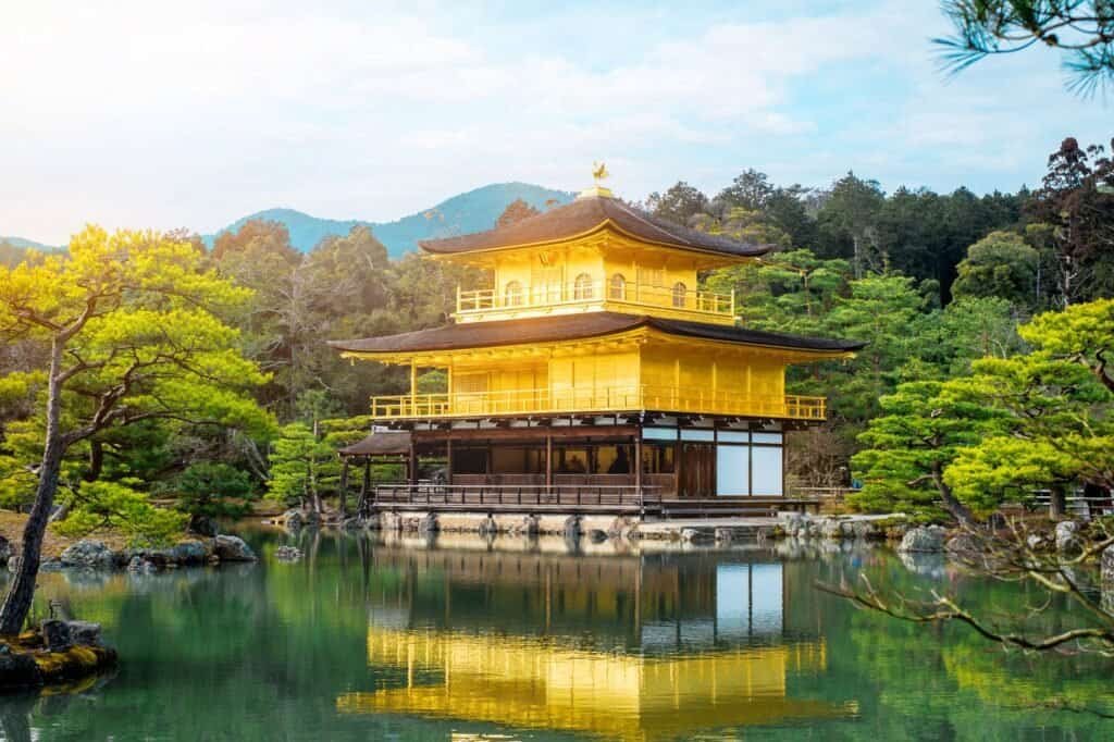 A golden temple stands beside a reflective pond, surrounded by lush greenery and mountains in the background, offering a luxury adventure travel experience.
