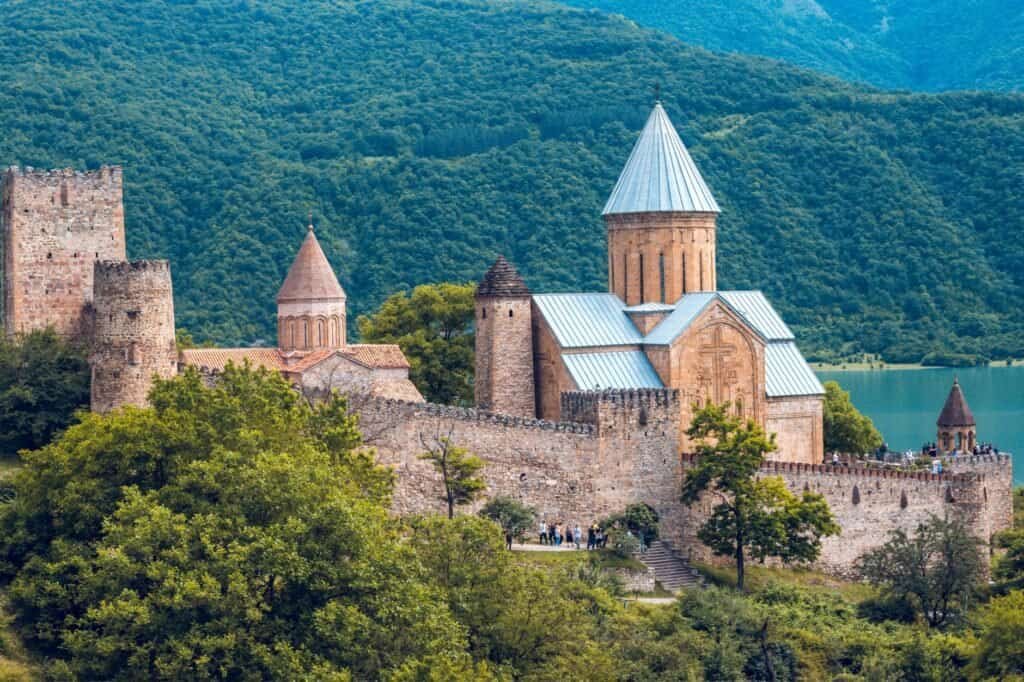 A historic stone fortress with towers and conical spires, set amidst lush green hills and overlooking a tranquil lake, offers the perfect backdrop for a luxury adventure.