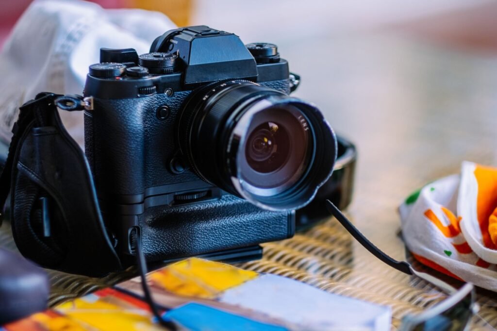 A black digital camera with a lens and strap sits on a wicker surface next to scattered papers and colorful fabric. travel photography tips