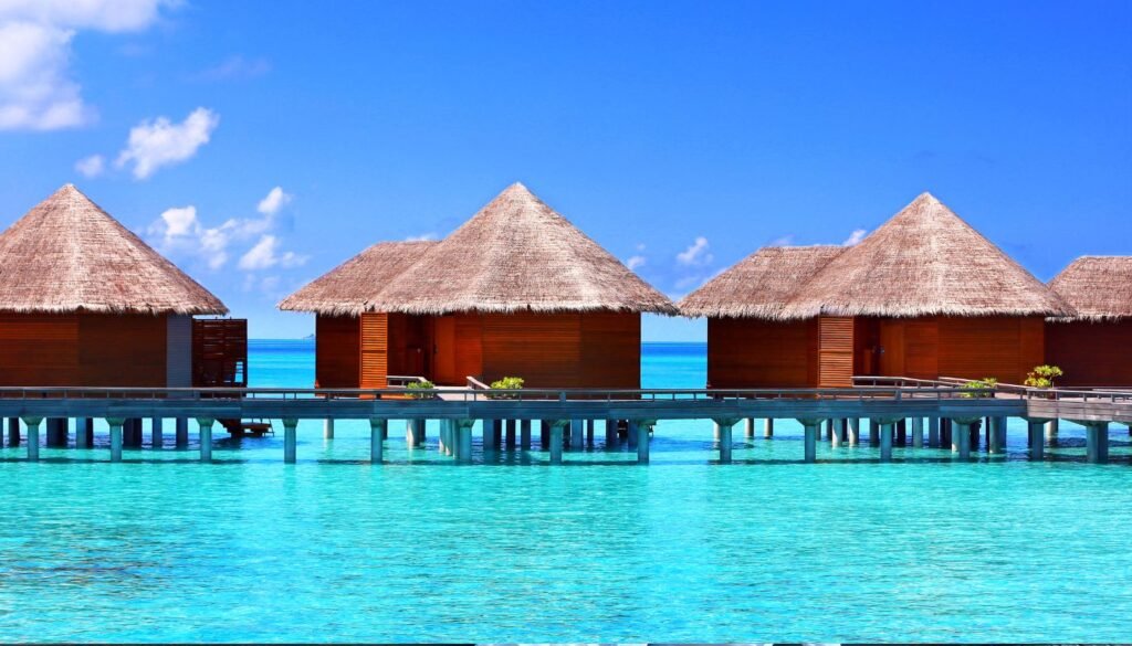Luxury travel reaches its pinnacle in overwater bungalows with thatched roofs, standing elegantly above clear turquoise waters under a bright blue sky.