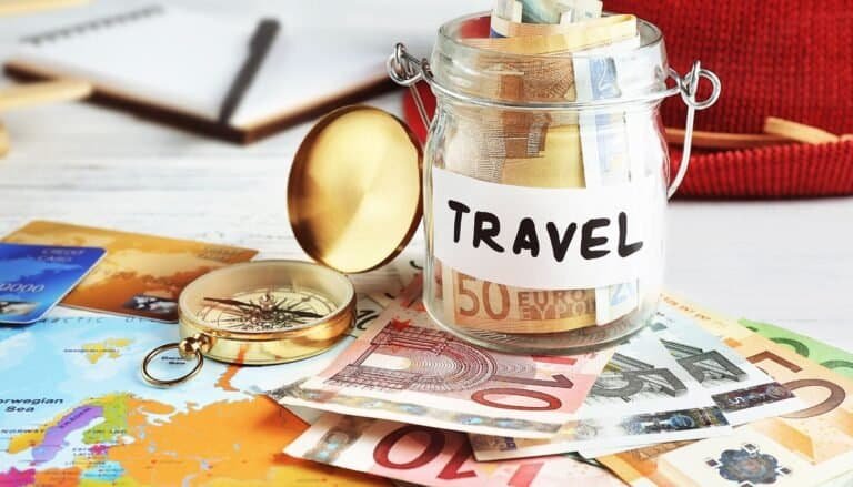 A jar labeled "Travel" filled with Euro notes, surrounded by a compass, map, and more Euro bills on the table—a perfect setup for budget travel enthusiasts plotting their next budget travel