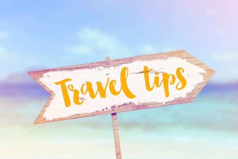 Wooden sign with "Essential Travel Tips" elegantly written in yellow script, set against a serene, blurred beach background.