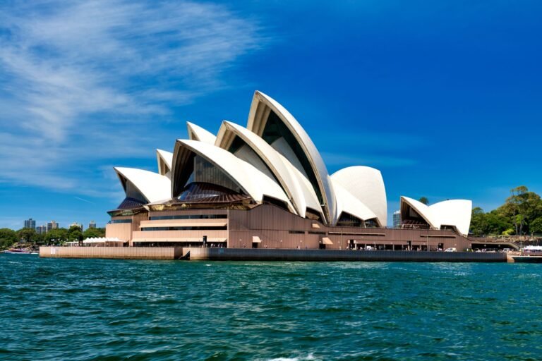 The Sydney Opera House, with its distinctive white sail-like shells against a clear blue sky, stands majestically viewed from the water. As featured in numerous destination guides, it's a must-see landmark that encapsulates the vibrant spirit of the city.