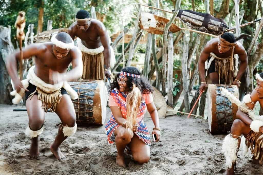 People in traditional clothing engage in a vibrant cultural adventure, dancing outdoors with the rhythmic beat of drums in the background.