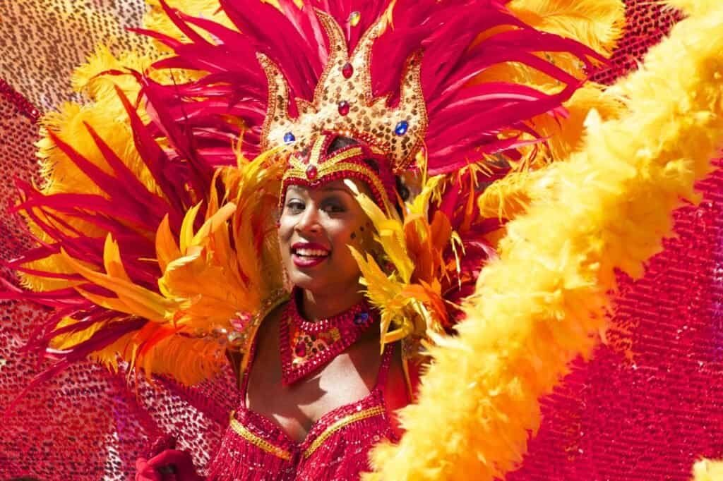 A person in a vibrant red and yellow feathered costume with a decorative crown, smiling radiantly against a similarly colorful background, embodies the spirit of cultural adventure.