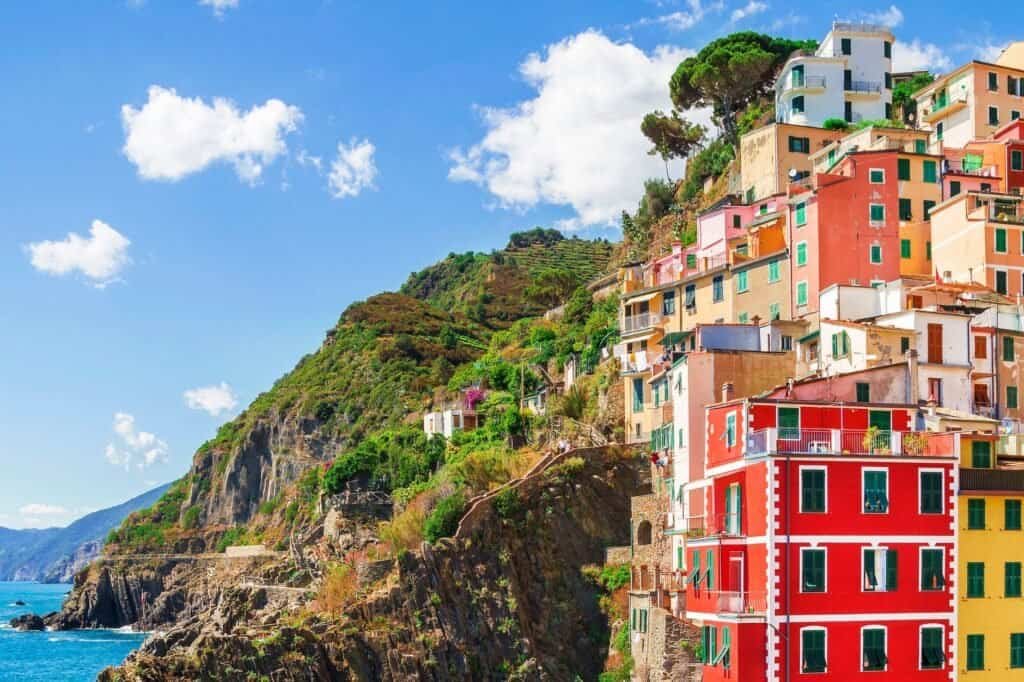 Colorful cliffside buildings along the coast in Cinque Terre, Italy, create a picturesque backdrop for a Fall Adventure Travel experience against the vibrant blue sky and sea.