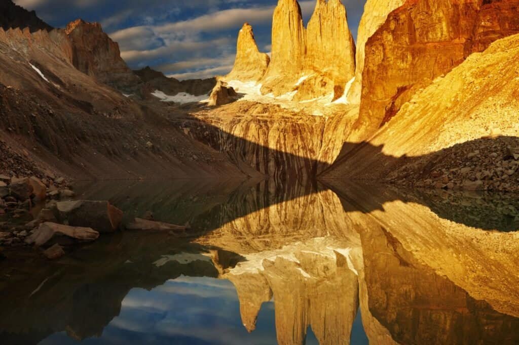 Golden rock formations reflected in a calm lake during sunset, surrounded by rocky terrain and a partly cloudy sky—a perfect spring adventure idea for nature enthusiasts seeking serene beauty.