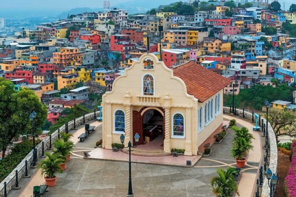 A small church on a hill overlooks a colorful hillside neighborhood, offering a picturesque view of the vibrant buildings below. It's one of those charming, cheap places to travel where every corner tells a story.