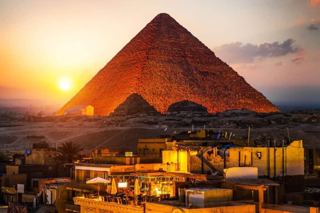 The Great Pyramid of Giza at sunset is a captivating destination, with buildings in the foreground and a cloudy sky, making it one of the most awe-inspiring yet surprisingly cheap places to travel.