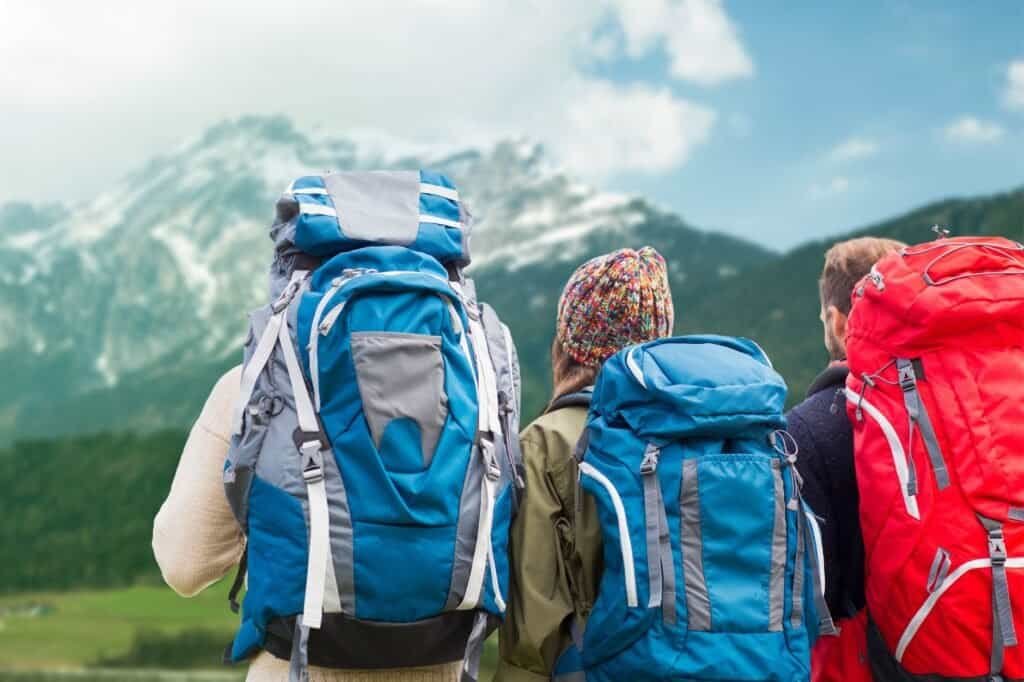 Three people with lightweight backpacks stand facing a mountain landscape, two with blue packs and one with a red pack.