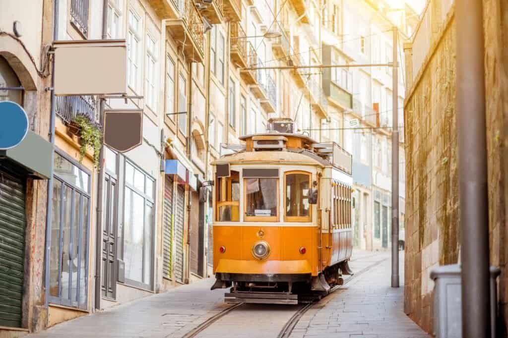 A vintage yellow tram glides on narrow tracks through a street lined with old buildings under a bright sky, offering a glimpse into one of the cheap places to travel in style.