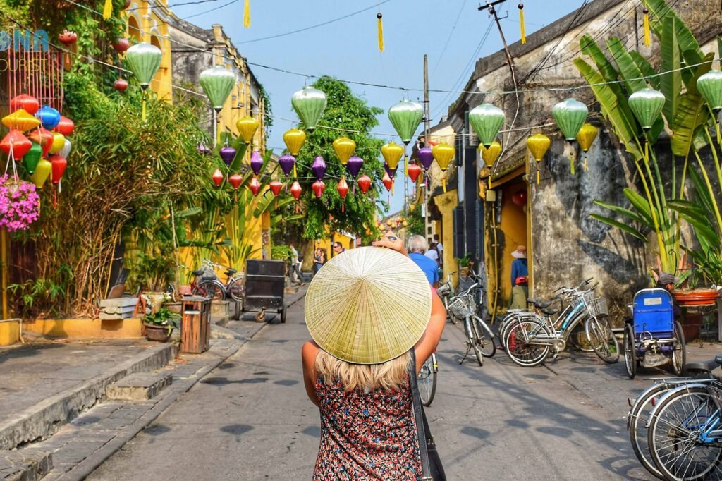 Strolling through a street adorned with colorful lanterns, a traveler in a conical hat discovers one of the world's cheap places to travel. Bicycles glide past old buildings, each corner whispering tales of history and adventure.