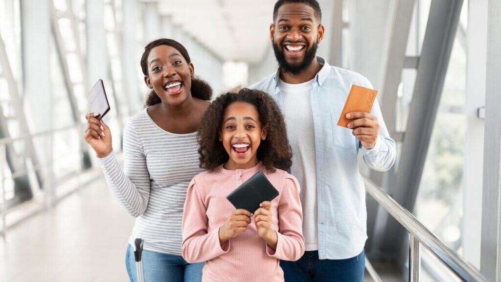 Three people stand indoors, smiling and holding travel documents, including passports. They appear happy and excited, possibly in an airport or travel setting, perhaps having just consulted a packing guide for budget family travel to make their journey smoother and more affordable.