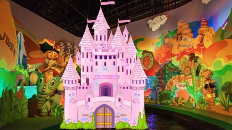 Colorful indoor amusement ride scene featuring whimsical dolls, vibrant wall art, and a large, pink cartoon castle at the center—perfect inspiration for those learning how to visit Disneyland on a budget.