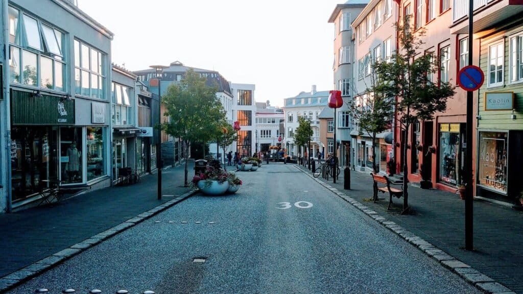 A quiet pedestrian street lined with shops and benches, with trees and large planters in the center, and buildings on both sides under clear daylight—an inviting spot for budget solo female travel.
