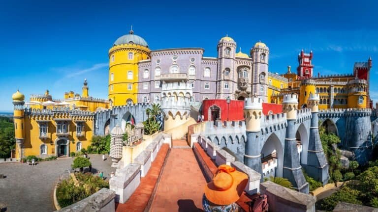 A panoramic view of Pena Palace in Sintra, Portugal, showcasing its colorful yellow, red, and purple façades under a clear blue sky—a must-see for budget solo female travel seeking vibrant and safe destinations.